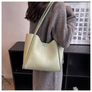 Rear view of a sage green faux leather tote bag worn by a model in a minimal interior