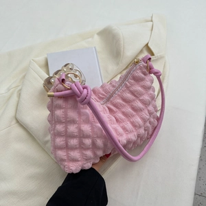 Pink bubble textured shoulder bag with knotted strap and gold hardware on beige suit