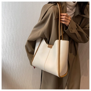 Detail of minimalist cream tote bag with brown leather trim worn with a trench coat