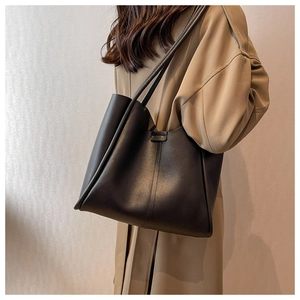 Side view of large black leather tote bag on model wearing a trench coat