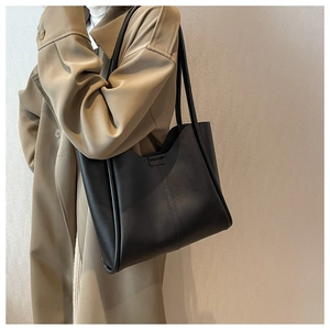 Minimalist black faux leather tote bag worn with trench coat for daily commuting