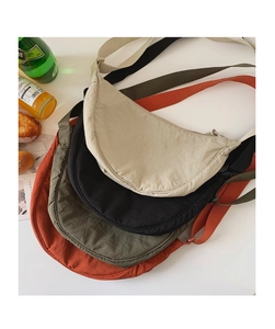 Variety of colorful nylon crescent crossbody bags arranged with lifestyle props on a white surface