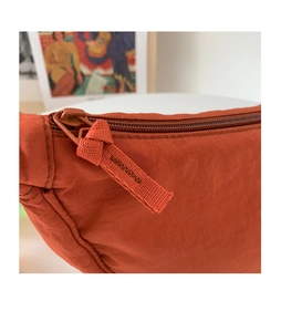 Macro detail of burnt orange nylon crossbody bag with matching zipper pull and fabric texture