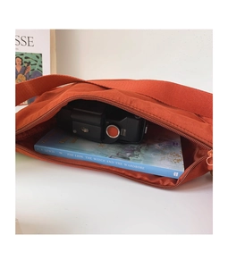 Macro view of rust red nylon crossbody bag showing interior capacity with book and camera