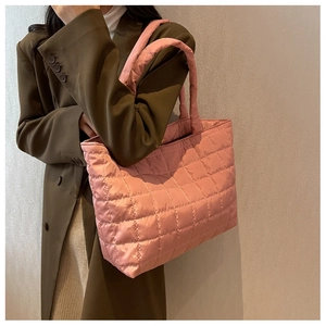 Detail of pink quilted puffer tote bag carried by a model in an olive green coat