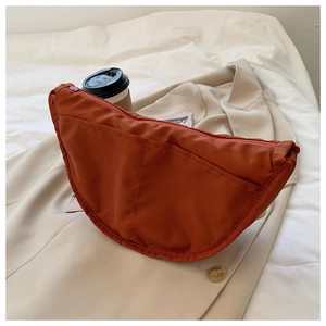 Detailed view of an orange nylon crescent crossbody bag styled on a beige trench coat