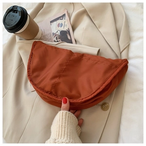 Detailed view of dark red nylon crescent moon bag on a trench coat with urban props