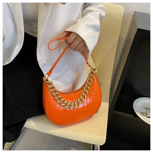 Orangefarbene Tasche mit Krokodilprägung und einer markanten klobigen Goldkette am Griff