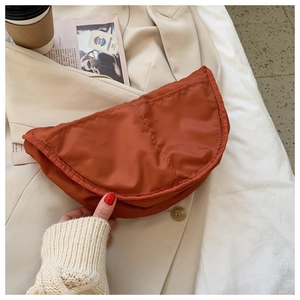 Burnt orange nylon half-moon crossbody bag held by a model in a minimalist urban setting