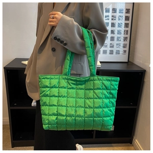 Close-up of bright green quilted nylon tote bag worn on shoulder by a fashion model