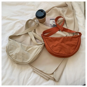 Flat lay of nylon crescent crossbody bags in beige and burnt orange on a bed
