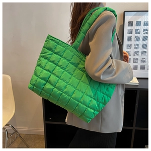 Detailed side view of a vibrant green quilted tote bag worn by a model in a gray suit