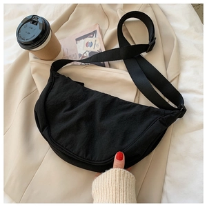 Macro view of black nylon crescent bag on beige suit with coffee and magazine props