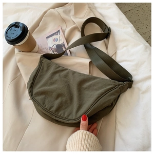 Detailed view of dark olive nylon crescent bag on a beige blazer with coffee and magazine