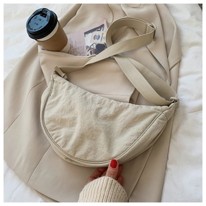 Minimalist beige crescent crossbody bag shown in a stylish lifestyle scene with natural texture