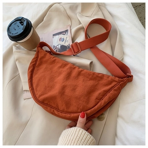 Detail of an orange nylon half-moon crossbody bag styled on a beige blazer jacket
