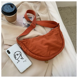Detail of orange nylon crescent bag with adjustable strap on beige blazer