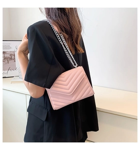 Detail of pink quilted crossbody bag with silver chain strap worn by a model