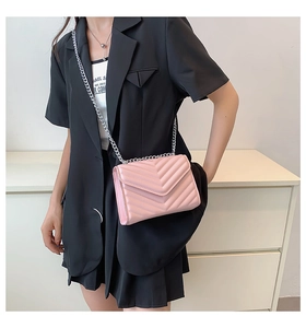 Close-up of pink chevron quilted leather crossbody bag with silver chain strap worn by model