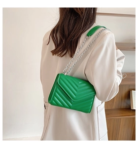 Detail of green V-quilted faux leather bag with silver chain strap worn by a model