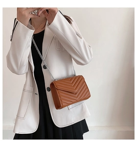 Brown crossbody bag with V-quilted texture and silver chain strap on white blazer model