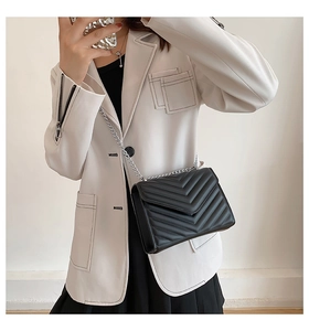 Detail of black quilted crossbody bag with silver chain strap and V-stitch pattern