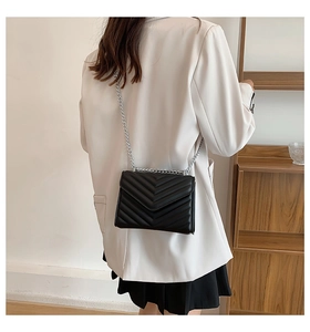 Model wearing a black V-quilted crossbody bag with silver chain strap on white blazer