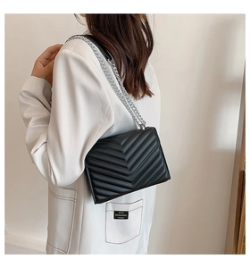 Detail view of black quilted crossbody bag with silver chain strap on model