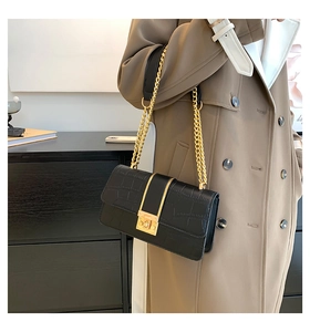 Detail van zwarte tas met krokodillenpatroon, gouden ketting en vierkante metalen slot