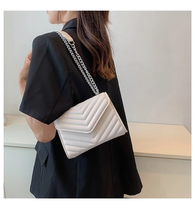Detail of white chevron quilted crossbody bag with silver chain strap on black blazer