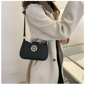 Détail d'un sac d'épaule noir matelassé avec fermoir doré porté sur un manteau beige