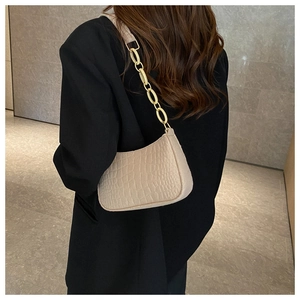 Detail of beige crocodile pattern baguette bag with bold gold chain strap on model