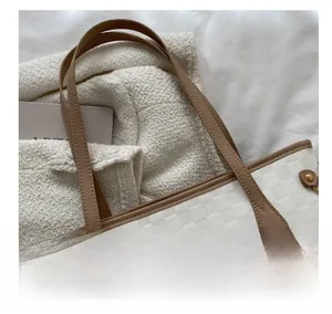 Detail of white quilted tote bag with brown leather handles and gold metal rivets