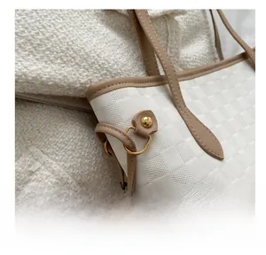 Detail of white woven checkerboard tote bag showing golden hardware and leather trim