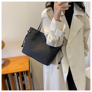 Close-up of black quilted tote bag with side drawstrings worn with a white trench coat