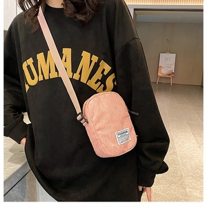 Pink corduroy mini crossbody bag with adjustable strap and decorative label detail