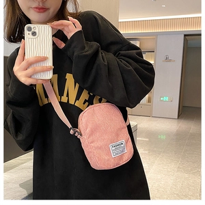 Pink corduroy crossbody bag featuring white fashion label and adjustable strap detail