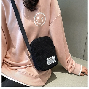 Detail of black corduroy crossbody phone bag with adjustable strap on pink hoodie