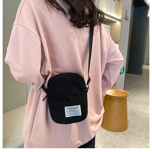 Detail showing a black corduroy mini crossbody bag worn by a model in an indoor setting