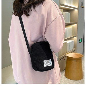 Detailed shot of a black corduroy crossbody phone bag worn by a person in a modern interior
