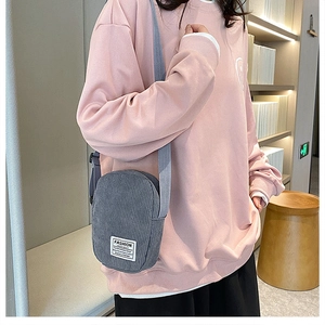 Close-up of grey corduroy crossbody bag with fashion label on a soft pink sweater