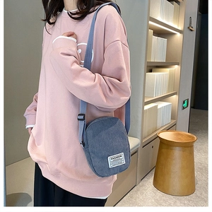 Blue corduroy small crossbody bag with fashion instinct label worn by a model in a pink hoodie
