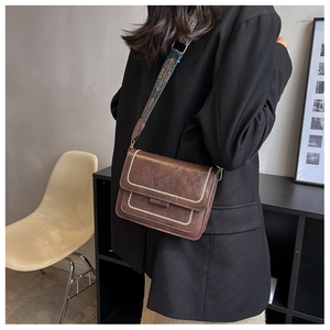 Close-up of vintage brown PU leather bag with metal rivets and blue geometric wide strap