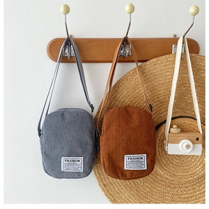 Detail of corduroy crossbody bags in gray and brown with fashion labels on a rack