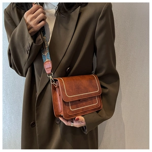Detail of vintage brown crossbody bag with white stitching and ethnic pattern wide strap