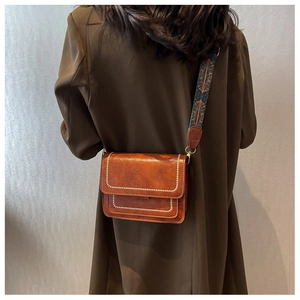 Detail of vintage brown crossbody bag with metal rivets and ethnic pattern wide strap