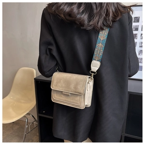 Detail of a beige leather crossbody bag with ethnic style wide printed strap worn by a model