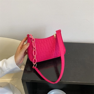 Crocodile embossed rose red shoulder bag with chunky chain strap on a black table