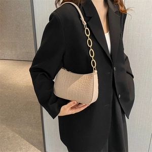 Beige crocodile embossed felt crossbody bag with gold chain strap on model's shoulder