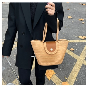 Detail of woven bucket bag with brown leather flap and pearl accent held by model